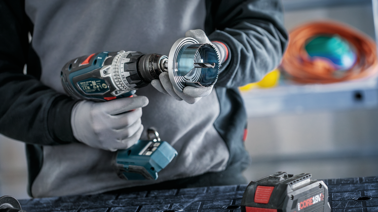 Person wearing safety equipment attaches a hole saw to a cordless drill.