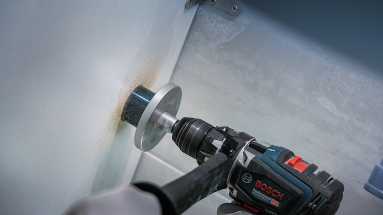 Person wearing safety equipment drills a hole in metal using a hole saw.