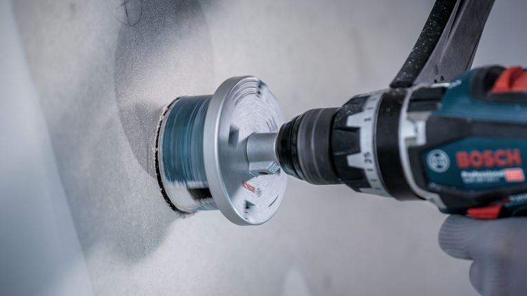 Person wearing safety equipment drilling a circular hole into a wall.
