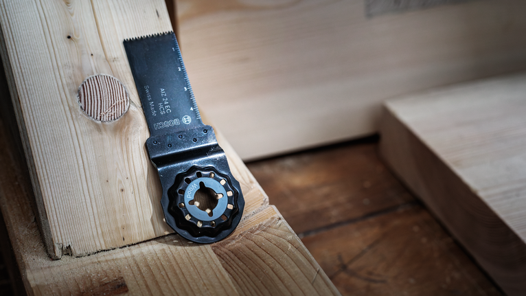 Oscillating saw blade rests on a wooden surface next to freshly cut wood.