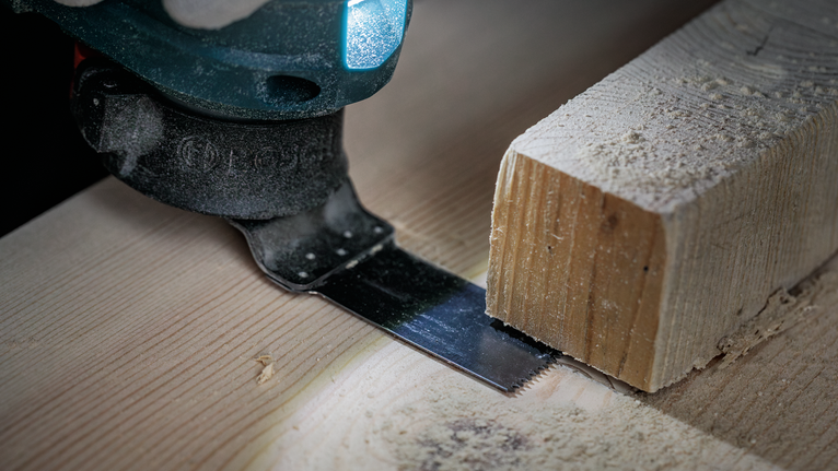 Oscillating saw blade cutting a wooden plank in a close-up workshop view.