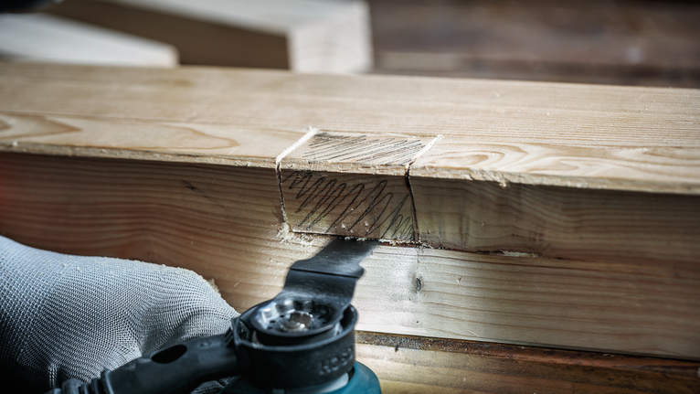 Person wearing safety equipment uses a power tool to cut a groove in a wooden beam.