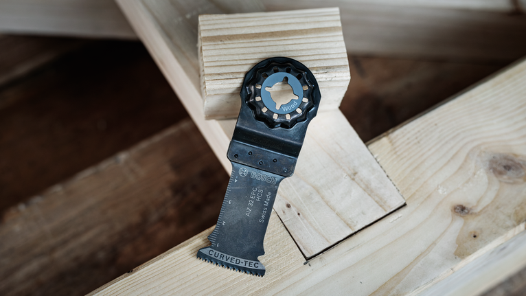 Oscillating saw blade placed on stacked wooden beams.