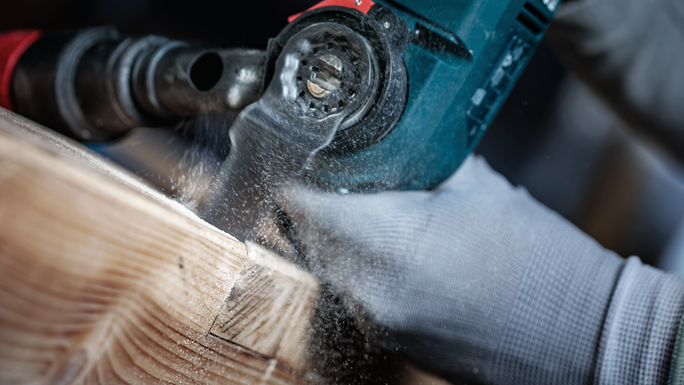 Person wearing safety equipment cutting wood with a power tool.