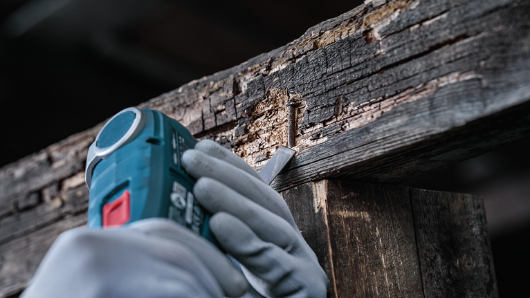 Person wearing safety equipment uses a power tool to extract a nail from damaged wood.