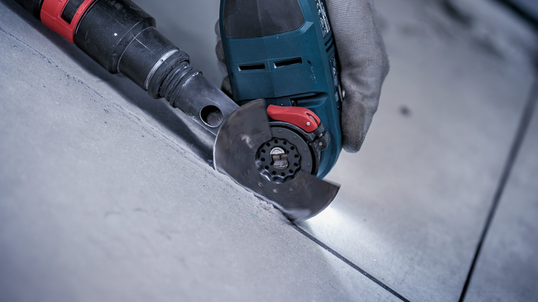 Person wearing safety equipment cuts a floor tile using a handheld power cutter.