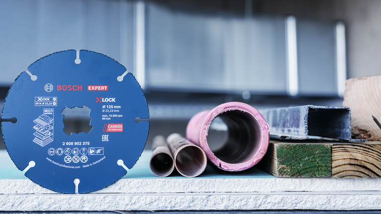 EXPERT Multi Material Carbide Cutting Disc, 125 x 22.23 mm, X-Lock Circular saw blade displayed upright beside metal pipes and construction materials.