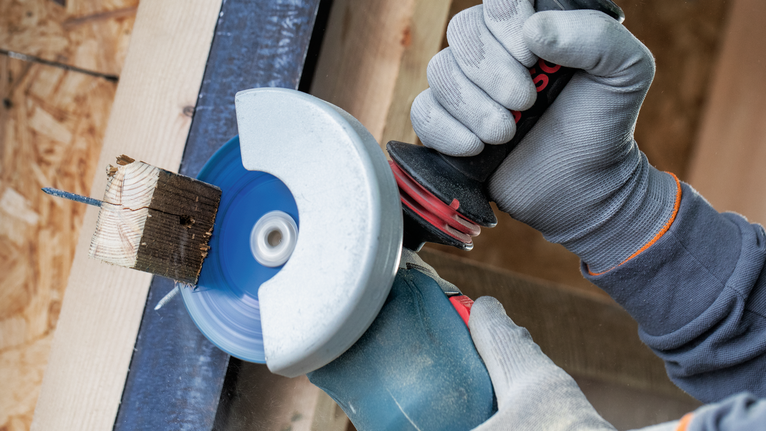 EXPERT Multi Material Carbide Cutting Disc, 125 x 22.23 mm, X-Lock Person wearing safety equipment grinds a nail embedded in a wood block.
