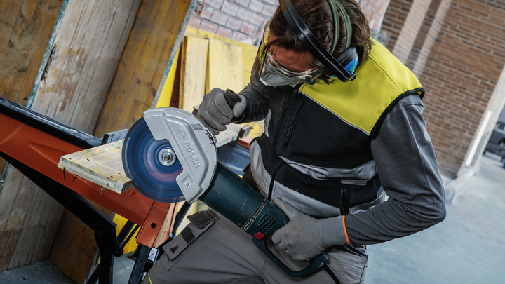 Object #200609273: 3065325_app_web_10 Person wearing safety equipment cuts a wooden plank with a large circular saw.