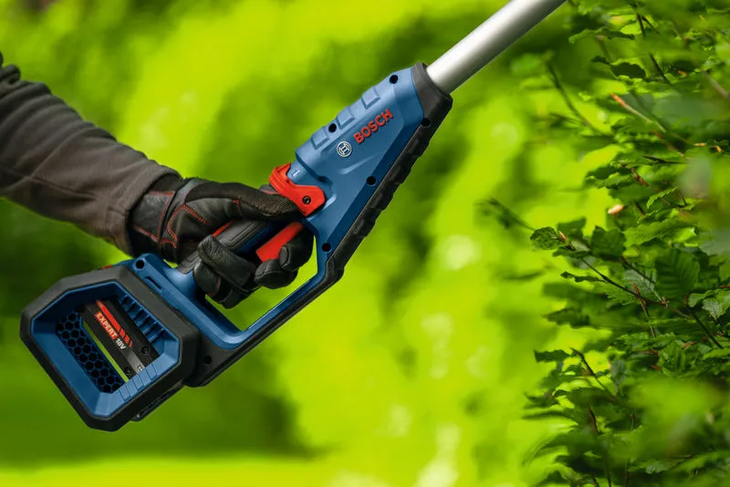 A person wearing safety equipment trims hedges with a cordless hedgecutter.