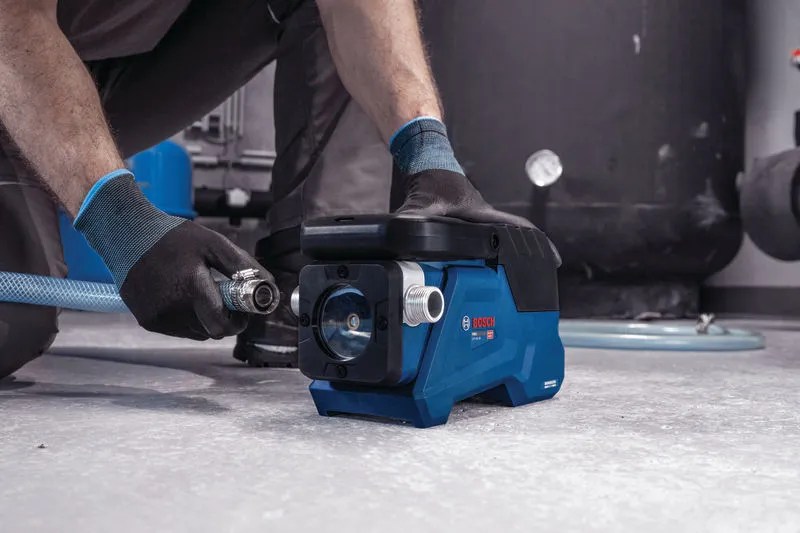 A person wearing safety equipment connects a hose to a compact blue water pump.