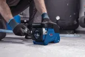 A person wearing safety equipment connects a hose to a compact blue water pump.