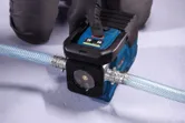 A person wearing safety equipment operates a portable water pump connected to a hose.