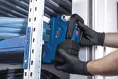 A person wearing safety equipment installs a blue power tool near metal shelving.