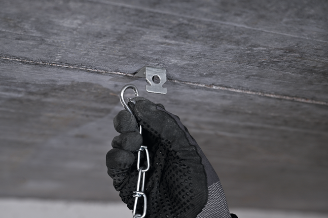 A person wearing safety equipment hooks a chain onto a metal ceiling hanger.