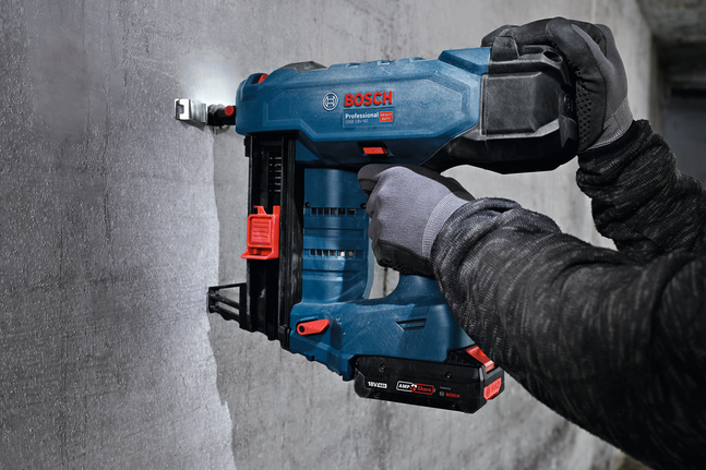 A person wearing safety equipment secures a metal cable tie mount to a concrete wall.