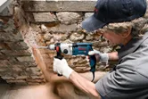 A person wearing safety equipment drills into a stone wall.