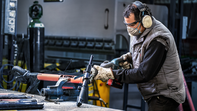 Person wearing safety equipment cuts a metal pipe with a reciprocating saw.