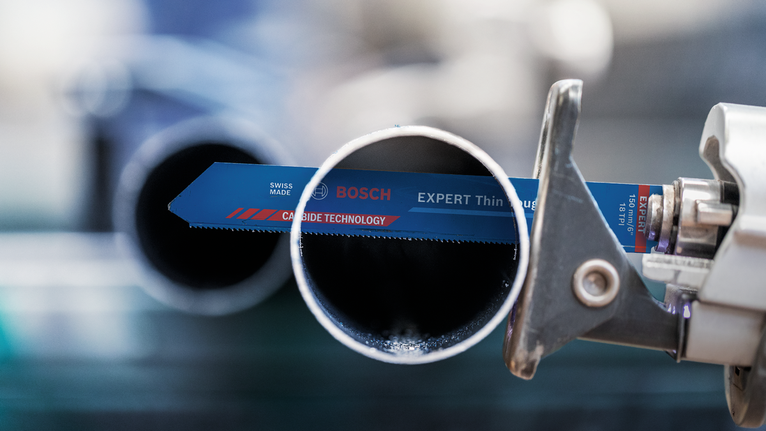 Saw blade cutting through a metal pipe in a workshop.