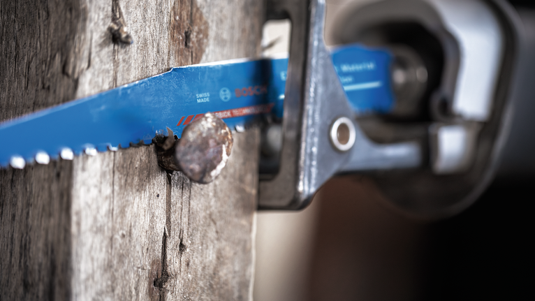 Reciprocating saw cutting through wood with a nail embedded.
