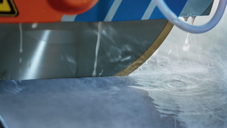 Circular saw blade with water cooling cuts through a stone slab.