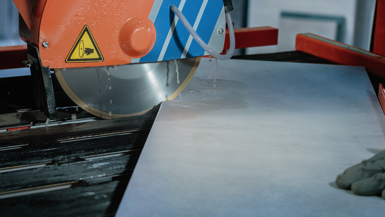A person wearing safety equipment cuts a tile with a wet saw.