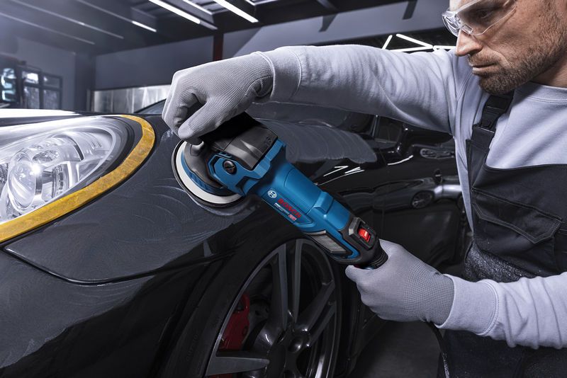 A person wearing safety equipment uses a polisher on a car fender.