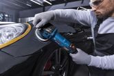 A person wearing safety equipment uses a polisher on a car fender.