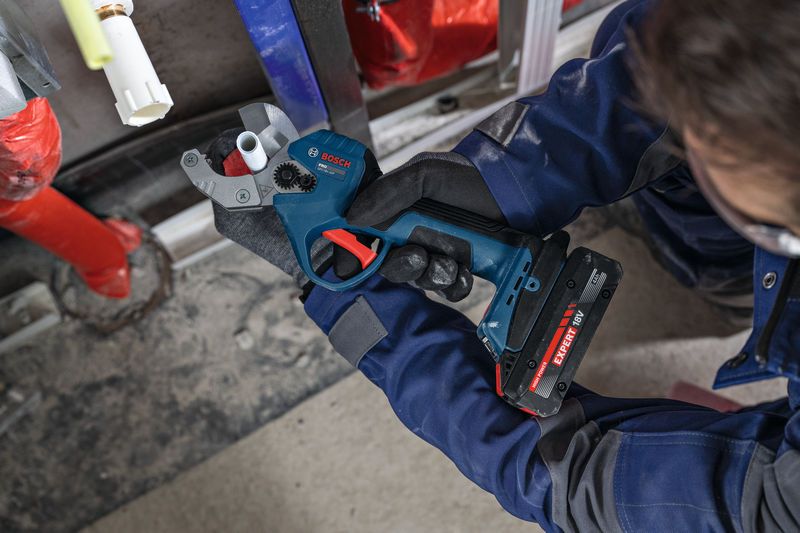 A person wearing safety equipment cuts plastic pipe with a cordless pipe shear.