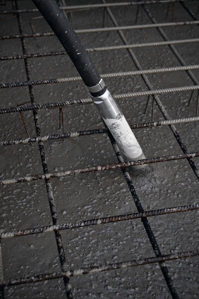 Concrete vibrator consolidating freshly poured concrete over a steel reinforcement grid.