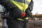 A person wearing safety equipment secures a belt while holding a concrete vibrator.