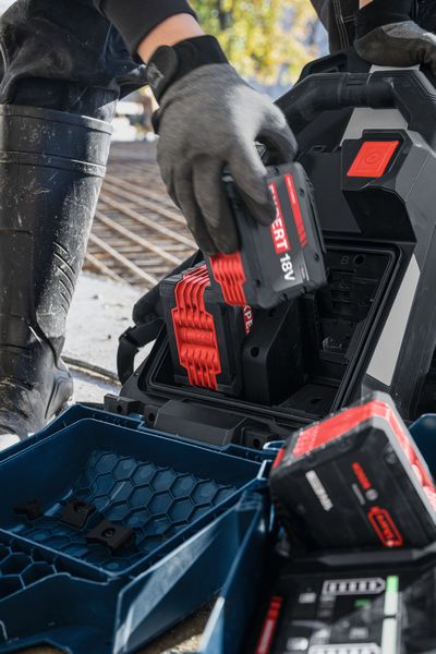 A person wearing safety equipment inserts a GPU18V2DI 18V battery into a charging station.