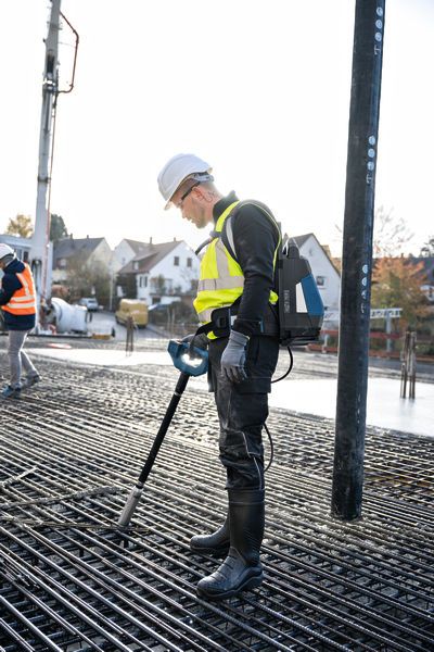 A person wearing safety equipment uses a concrete vibrator on a rebar grid.