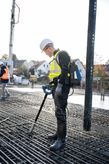 A person wearing safety equipment uses a concrete vibrator on a rebar grid.