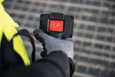 Person wearing safety equipment holds a device with a large red power button.