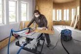 A person wearing safety equipment cuts wood on a table saw in a workshop.