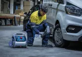 A person wearing safety equipment inflates a van tire using a portable air compressor.