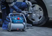 A person wearing safety equipment uses an air compressor to clean a car wheel.