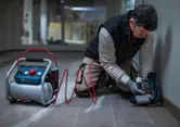 A person wearing safety equipment uses a pneumatic tool to fasten trim along a wall.
