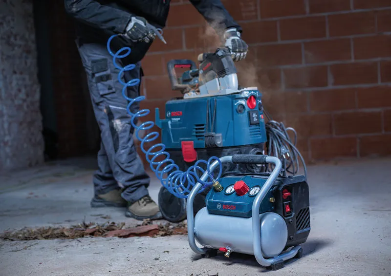 A person wearing safety equipment uses a portable air compressor connected to a saw.