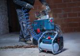 A person wearing safety equipment uses a portable air compressor connected to a saw.