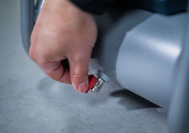 A person turns a red valve on a gray cylindrical machine.