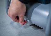 A person turns a red valve on a gray cylindrical machine.