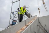 A person wearing safety equipment uses a power tool on a concrete staircase at a construction site.