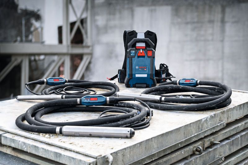 Concrete vibration tools with long black hoses and a control unit placed on a metal surface.