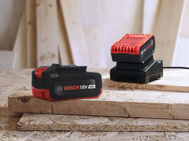 Rechargeable power tool battery and charger resting on stacked wooden boards.