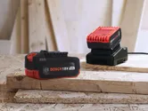 Rechargeable power tool battery and charger resting on stacked wooden boards.