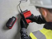 Person wearing safety equipment inserts a red battery into a charger on a concrete floor.