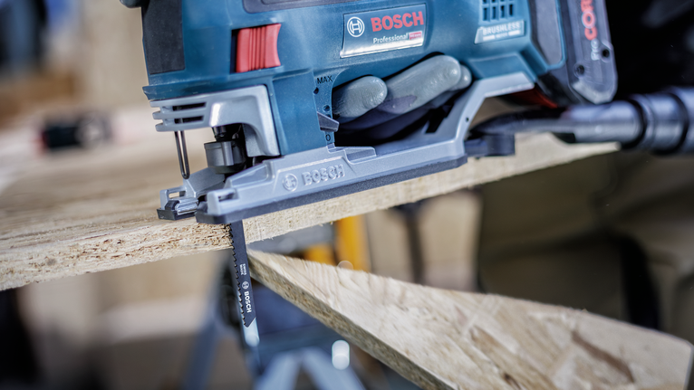 Person wearing safety equipment cuts wood with a blue jigsaw.