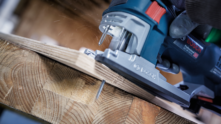Person wearing safety equipment cuts a wooden board with a jigsaw.